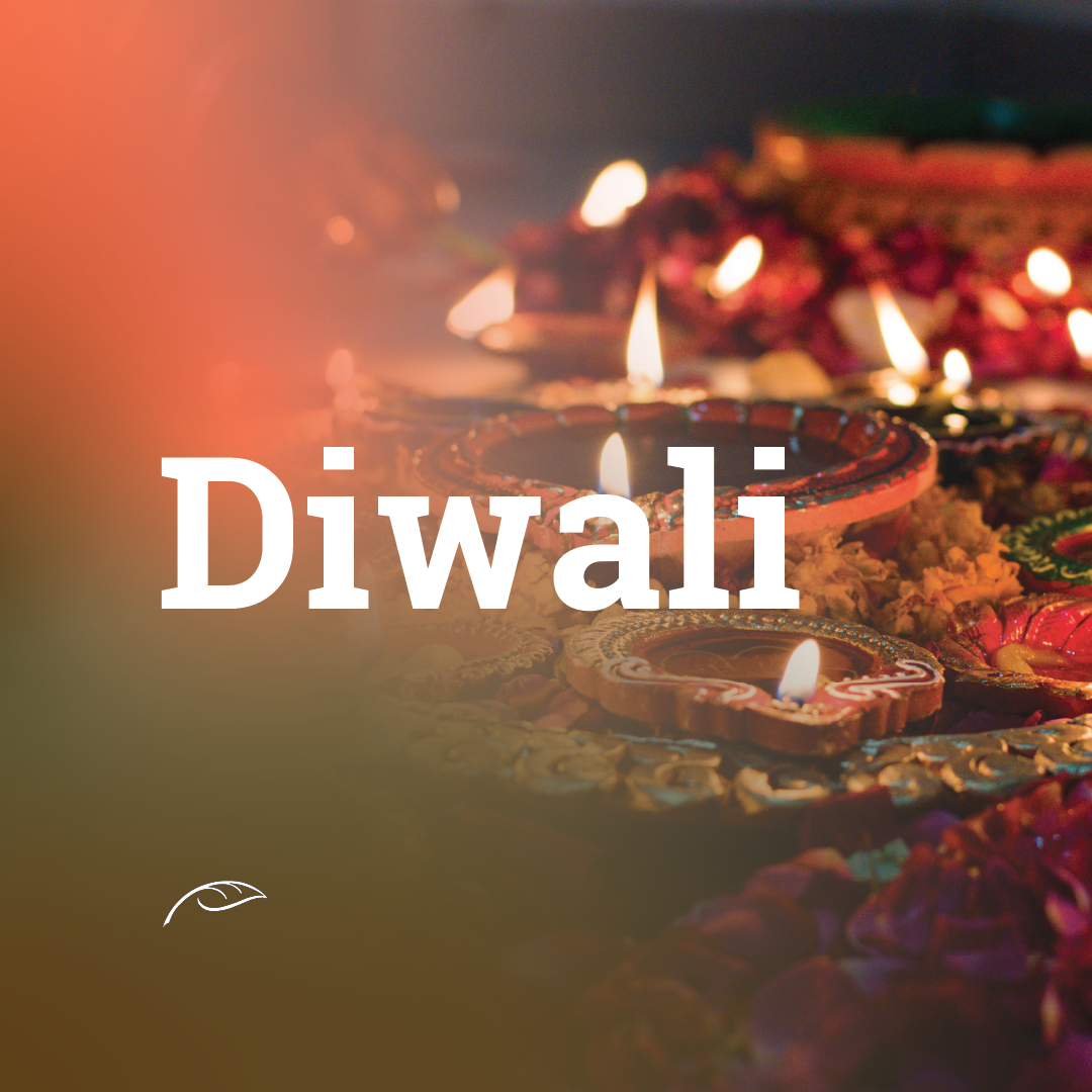 Decorative clay oil lamps (diyas) with glowing flames arranged among colourful floral decorations, with the word “Diwali” displayed prominently in white text.